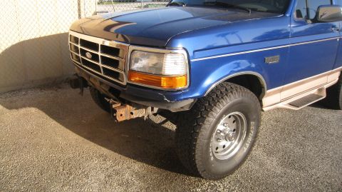 1996 Ford Bronco - The front quarter view of a blue Ford Bronco shows damage to the front bumper area. The vehicle is parked on a gravel surface next to a con…