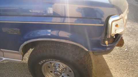 1996 Ford Bronco - A close-up view of the front driver's side fender and wheel of a blue Ford Bronco. The vehicle has a chrome trim around the wheel well and…