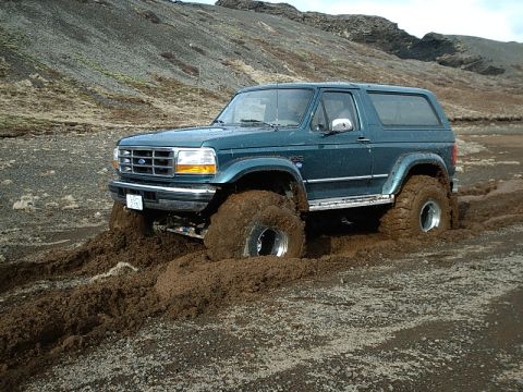 1996 Ford Bronco - A green 1996 Ford Bronco navigates challenging terrain, its large tires sinking into thick mud.