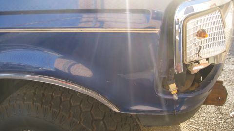 1996 Ford Bronco - Close-up of the front fender and damaged headlight assembly of a blue Ford Bronco. The vehicle has a chrome trim piece along the fender and…