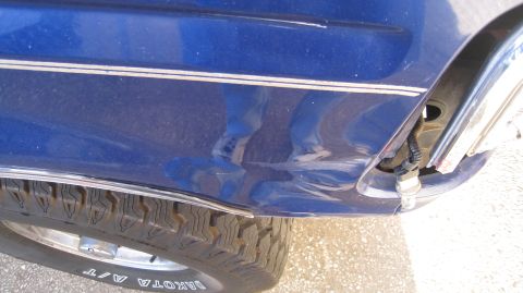 1996 Ford Bronco - A close-up view shows damage to the rear quarter panel of a blue vehicle, with a chrome trim piece and a tire visible below. A light bulb a…
