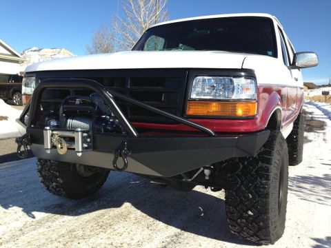 1996 Ford Bronco - A white and red Ford Bronco with a custom black front bumper and winch is parked on a snowy road. The vehicle is viewed from a low angle, f…