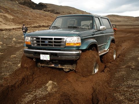 1996 Ford Bronco - A green 1996 Ford Bronco is stuck deep in mud, with its tires almost completely submerged.