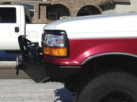 1996 Ford Bronco - A close-up, side-angle view of the front fender and bumper of a red and white Ford truck. A black aftermarket bumper with a winch mount is…