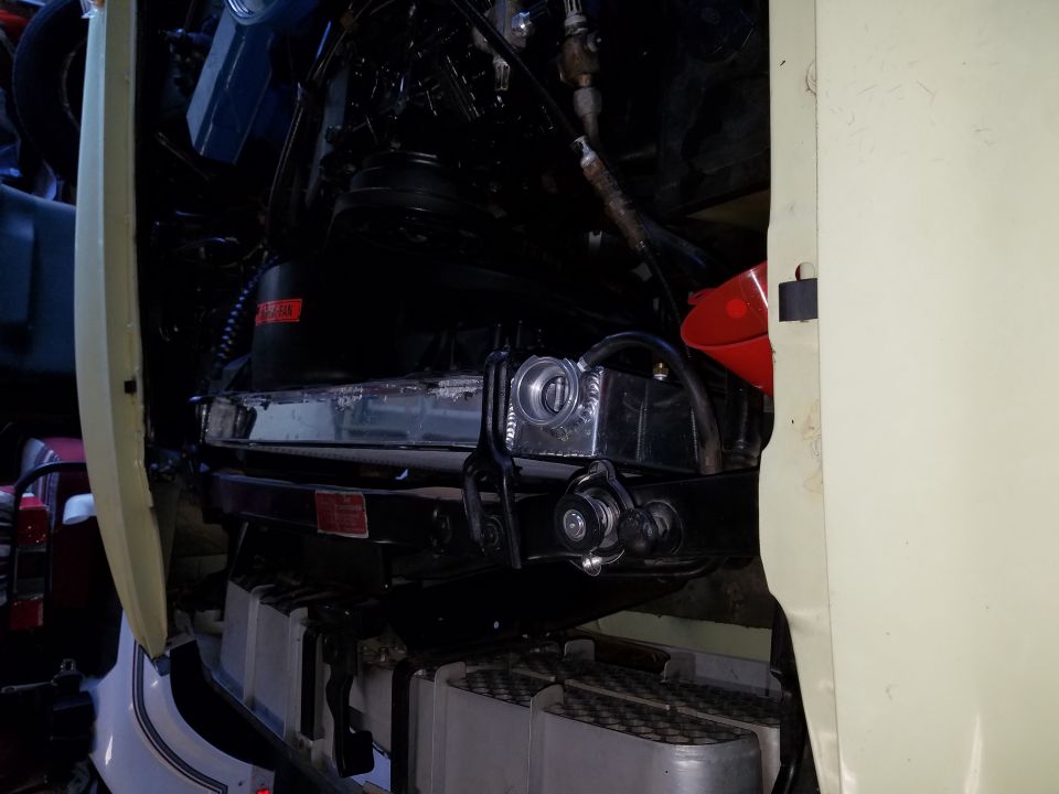 Engine bay of a vehicle with radiator and engine parts visible, red funnel present.