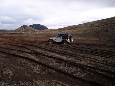 1996 Ford Bronco - A white Jeep Wrangler is stuck in the mud on a desolate, hilly landscape.
