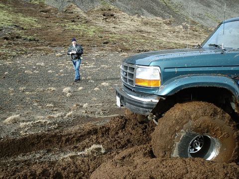 1996 Ford Bronco - A green Ford F-Series truck is stuck in thick mud off-road, with a person standing in the distance.