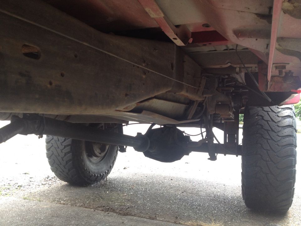Underside of a red Ford F-350 pickup truck showing frame, suspension, and tires.