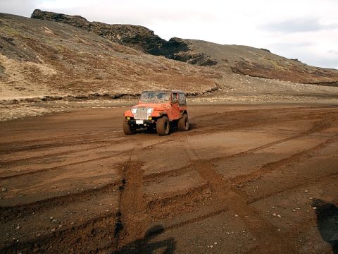 1996 Ford Bronco - Orange Jeep CJ-7 navigates a dirt track in a barren, hilly landscape.