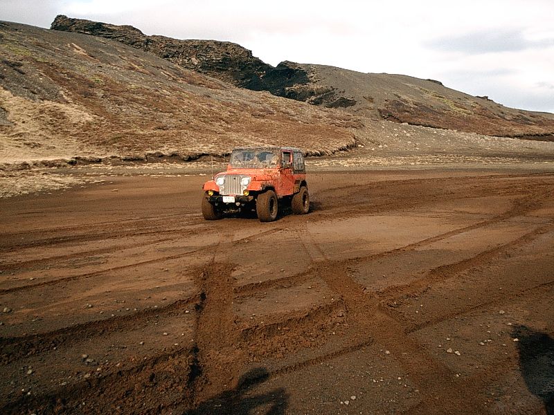 Orange open-top 4x4 with large tires on red volcanic sand near barren hills