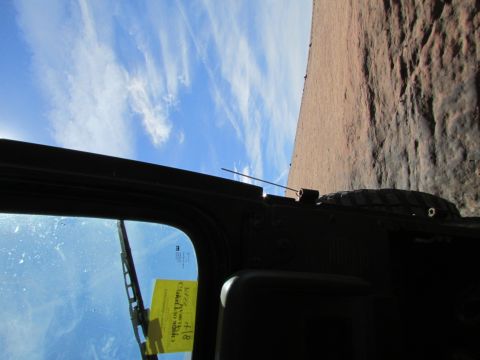 1995 Jeep Wrangler - View from inside a vehicle looking out the windshield at a rocky cliff face and blue sky with wispy clouds. A yellow sticker with writing i…