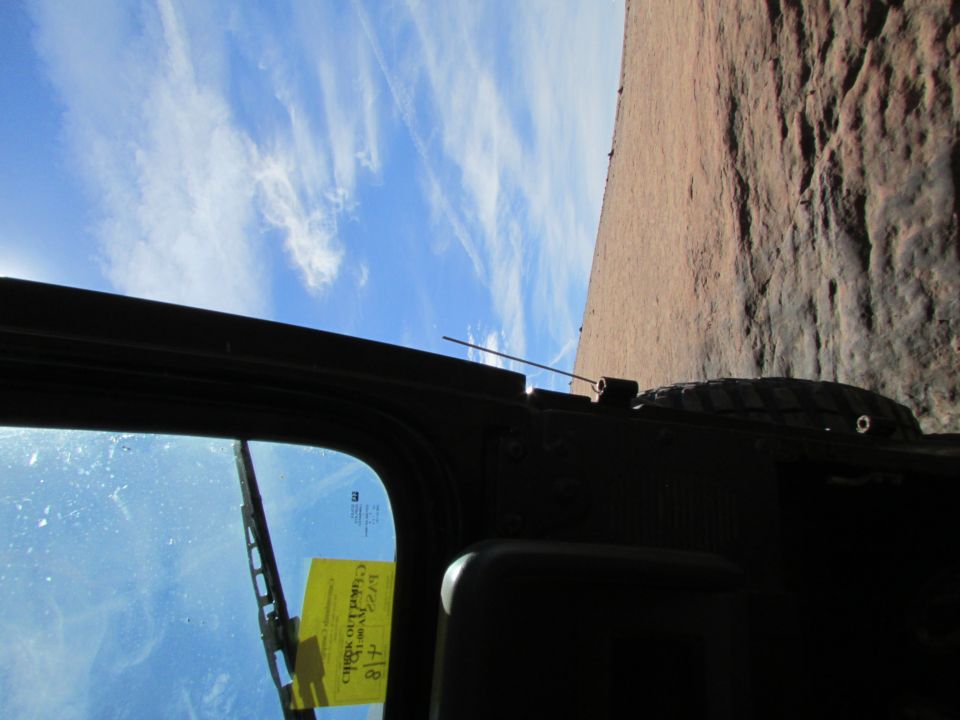 View from inside a vehicle looking out the windshield at a rocky cliff face and blue sky.
