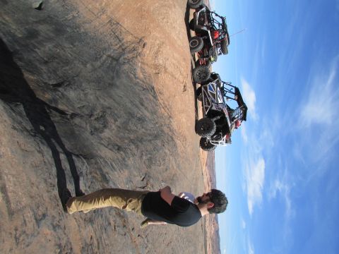 1995 Jeep Wrangler - Two side-by-side UTVs are parked on a rocky, desert-like terrain with a bright blue sky overhead. A person is visible in the foreground, fa…