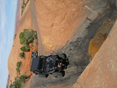 1995 Jeep Wrangler - Two black Jeep Wranglers navigate a rocky, desert terrain with sparse vegetation. The foreground Jeep is a YJ model, viewed from the rear t…