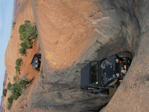 1995 Jeep Wrangler - Two black Jeep YJs navigate a narrow, rocky canyon with water on the ground. The Jeep in the foreground is angled steeply, showing its fron…