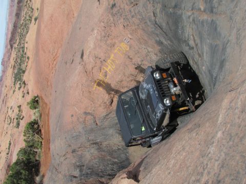 1995 Jeep Wrangler - A black Jeep YJ is precariously positioned in a narrow rock crevice, with yellow spray paint reading "THE HOT TUB" visible on the surroundi…