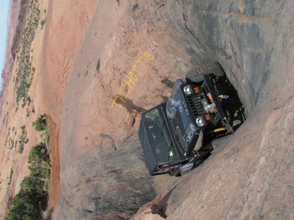 Black Jeep YJ tilted in a narrow rock crevice with yellow text on rock.