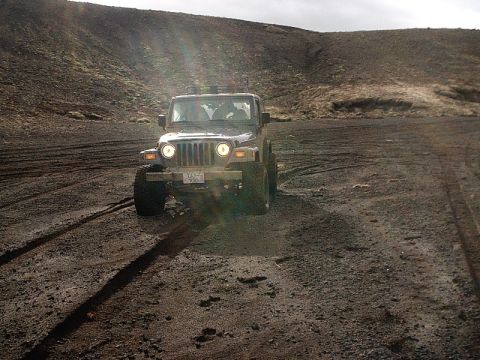 1996 Ford Bronco - A Jeep Wrangler navigates a rough, muddy terrain under an overcast sky.