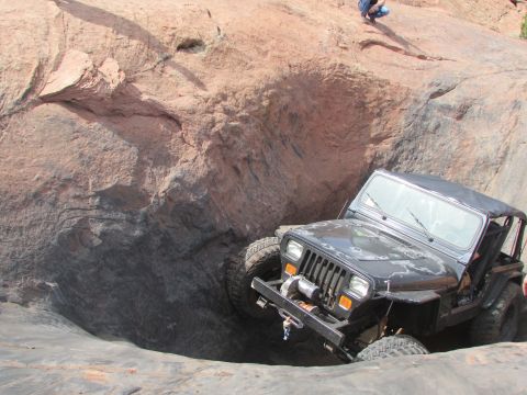 1995 Jeep Wrangler - A black Jeep YJ is navigating a steep, rocky descent. The vehicle is angled sharply, with its front tires pointed downwards into a crevice.