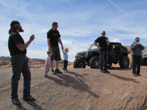 1995 Jeep Wrangler - A group of people stand on a rocky outcrop with a modified black Jeep Wrangler parked behind them. The Jeep has large off-road tires and ap…