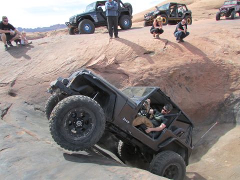 1995 Jeep Wrangler - A black Jeep YJ is navigating a steep, rocky incline with its front wheels elevated. Several people are observing the off-road maneuver fro…