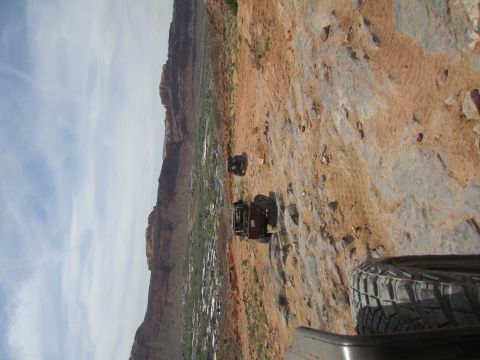 1995 Jeep Wrangler - A red Jeep Wrangler is parked on a rocky, off-road trail overlooking a valley with a town below. Another Jeep is visible further up the tra…