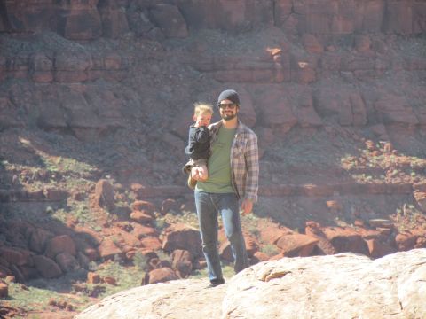 1995 Jeep Wrangler - A man holds a young child on his shoulders while standing on a rock formation in a desert landscape with red rock cliffs in the background.