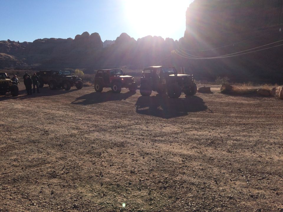 Several Jeep Wranglers parked in a desert landscape with mountains and bright sun.