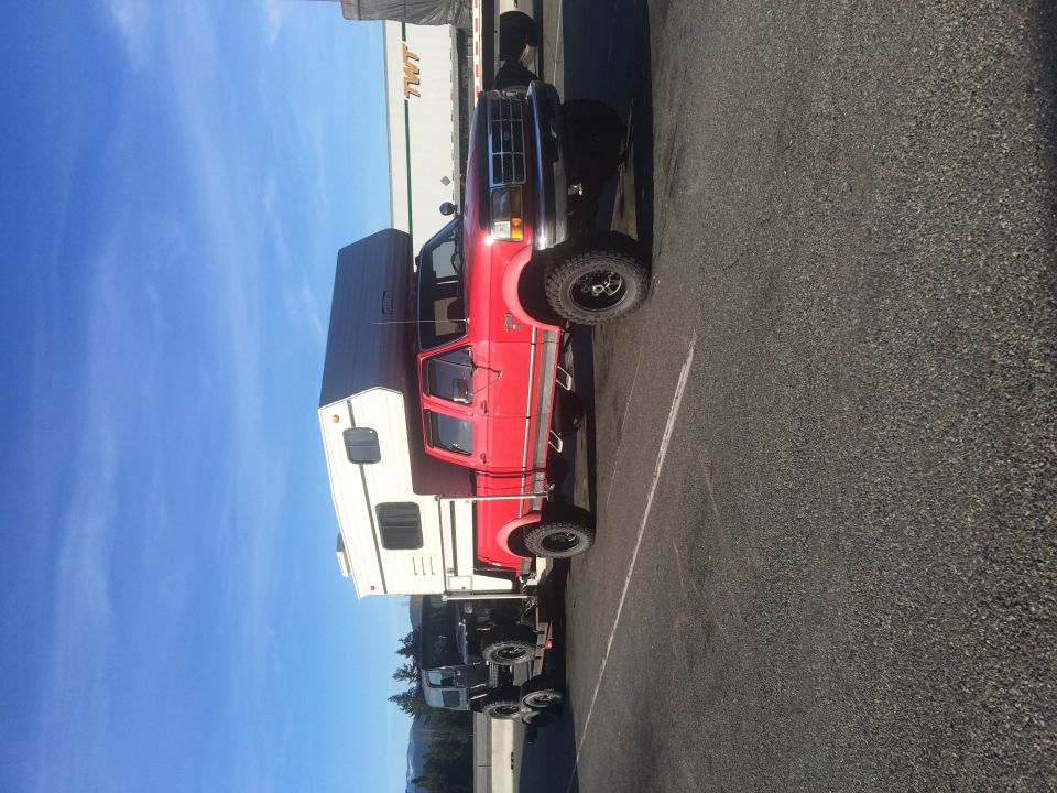 Red pickup truck with camper shell and off-road tires parked on asphalt.