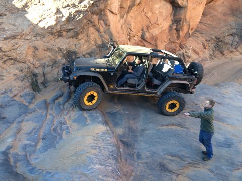1995 Jeep Wrangler - A black Jeep Wrangler Rubicon is parked on a rocky, off-road trail with a person standing to the right, pointing towards the vehicle. The J…