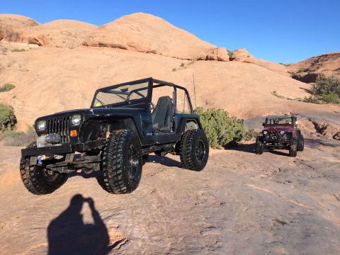 1995 Jeep Wrangler - A black Jeep YJ is parked on a rocky, desert landscape with a red Jeep Wrangler in the background. The vehicle is a two-door convertible wi…