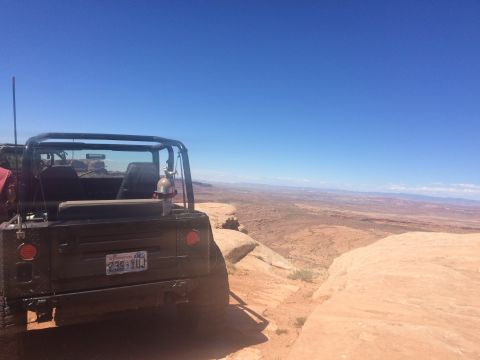1995 Jeep Wrangler - The rear of a black Jeep YJ is parked on the edge of a rocky cliff overlooking a vast desert landscape under a clear blue sky. A Washington…
