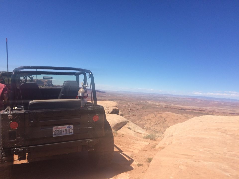 Rear view of a black Jeep YJ parked on a cliff edge with a desert landscape in the background. Washington license plate visible.