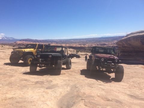 1995 Jeep Wrangler - Three modified Jeep Wranglers are parked on a rocky, desert landscape under a clear blue sky. The vehicles are a yellow YJ, a black TJ or Y…