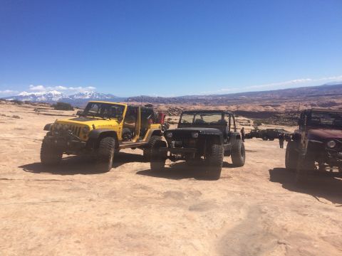 1995 Jeep Wrangler - Three off-road modified Jeeps are parked on a rocky, desert terrain under a clear blue sky. The Jeep in the foreground left is yellow, whil…