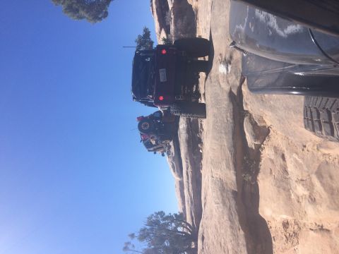 1995 Jeep Wrangler - Two modified Jeep Wranglers are shown navigating a steep, rocky trail under a clear blue sky. The lead Jeep is dark red, and the second Jee…