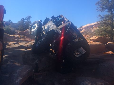 1995 Jeep Wrangler - A modified Jeep YJ is angled precariously on a rocky, off-road trail under a clear blue sky. The vehicle's large tires and lifted suspensio…