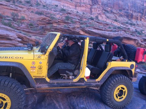 1995 Jeep Wrangler - A yellow Jeep Wrangler Unlimited is parked on a rocky trail with a canyon wall in the background. The driver is visible behind the wheel, a…