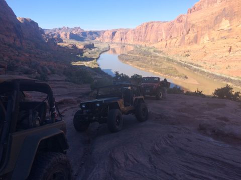 1995 Jeep Wrangler - Three Jeep Wranglers are parked on a rocky trail overlooking a river canyon. The lead Jeep is a dark color, followed by a red Jeep, and a t…