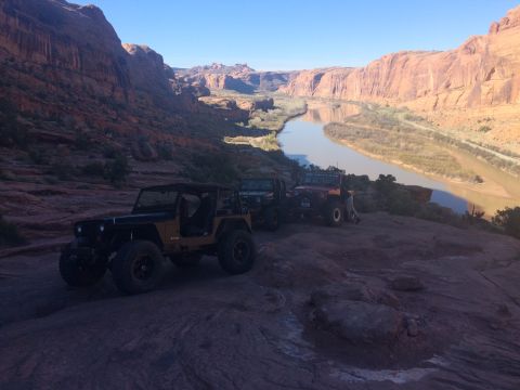 1995 Jeep Wrangler - Two Jeep Wranglers are parked on a rocky overlook with a river and canyon in the background. The Jeep in the foreground is black and tan wi…