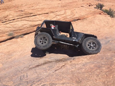 1995 Jeep Wrangler - A black Jeep YJ is navigating a steep, rocky incline in a desert environment. The vehicle is angled with its front wheels higher than its r…
