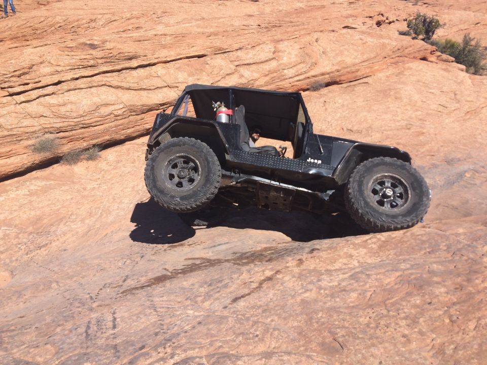 Black Jeep YJ off-roading on a steep, rocky desert terrain.