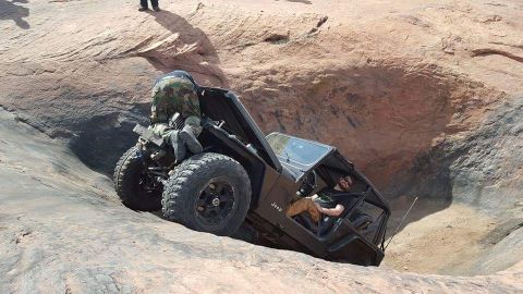 1995 Jeep Wrangler - A black Jeep YJ is tilted precariously on a rocky incline with one person on the exterior and another in the driver's seat.
