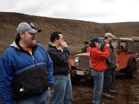 1996 Ford Bronco - Several people observe a muddy off-road vehicle in a desolate, hilly landscape.