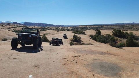 1995 Jeep Wrangler - A black Jeep YJ is parked on a rocky, desert landscape with other Jeeps in the distance. The vehicle is facing the camera at a three-quarte…