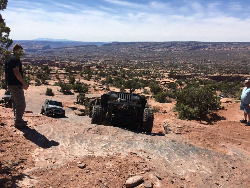 Two modified Jeep Wranglers on a rocky off-road trail with a desert canyon vista.