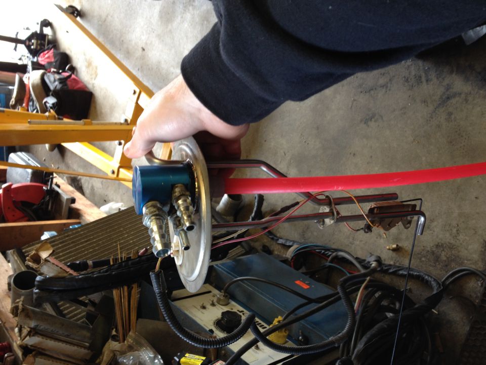 Fuel sending unit with red fuel line and brass fittings, held by a hand.