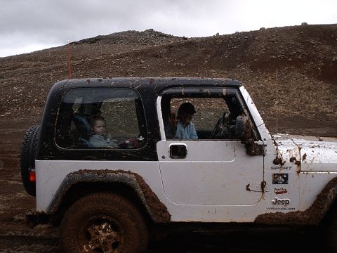 1996 Ford Bronco - A muddy Jeep Wrangler with two children inside drives through a desolate, rocky landscape.