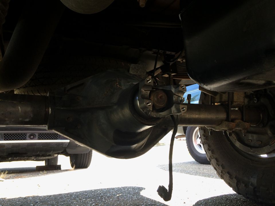 Underside of a vehicle showing rear differential, driveshaft, and hanging electrical connector.