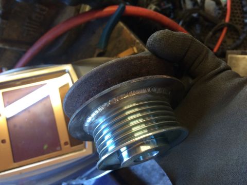 1995 Jeep Wrangler - A gloved hand holds a ribbed pulley with a welded flange. The pulley is shiny and metallic, with visible weld marks around the flange.